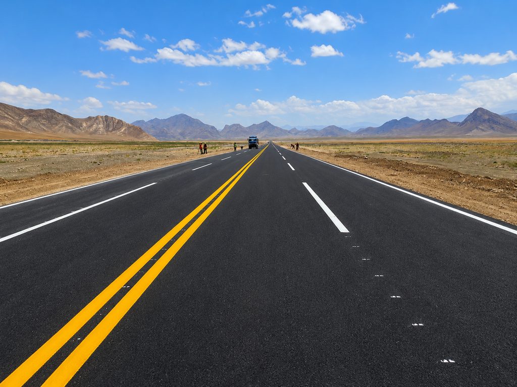 Newly paved asphalt access road to Aynak copper mine, Logar province, with mountains in the distance.