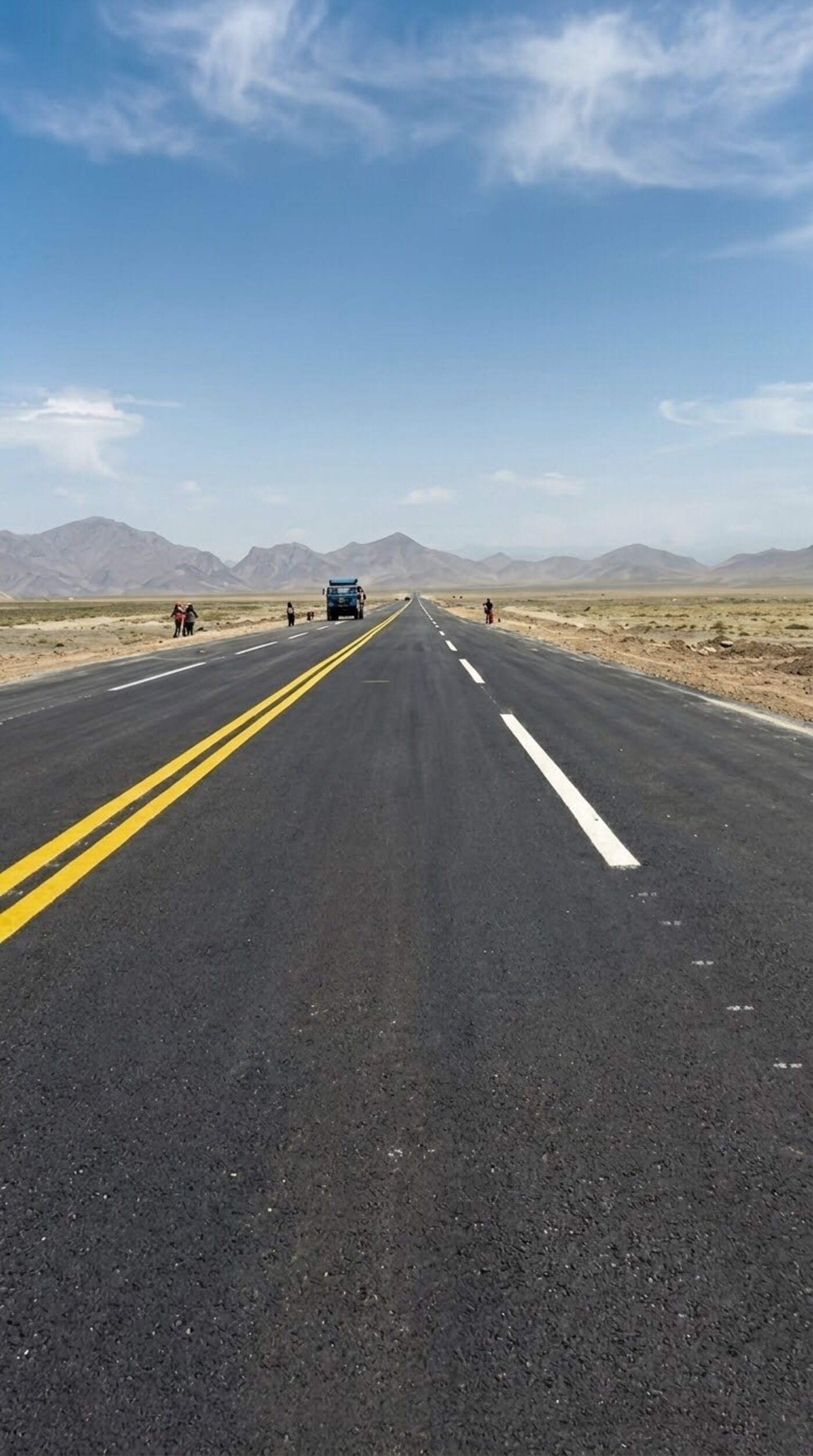Completed asphalt highway with double yellow centre line running toward mountains on the Aynak copper mine access road in Logar province