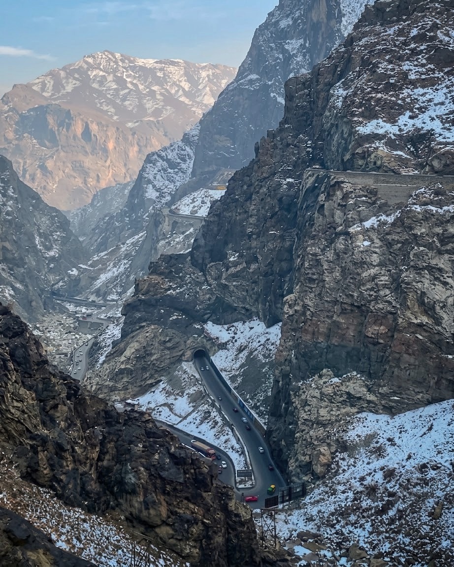 The Kabul to Jalalabad highway climbing through a snow-dusted rock gorge with traffic moving along the carriageway